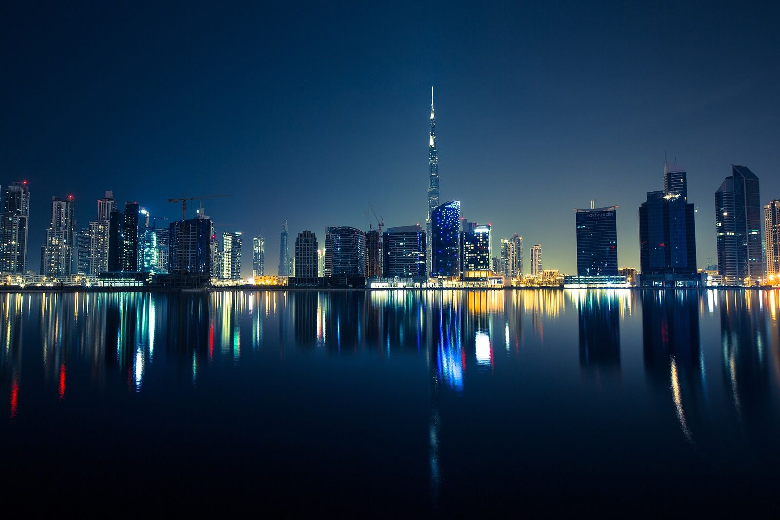 The Dubai skyline at night, reflected in still water