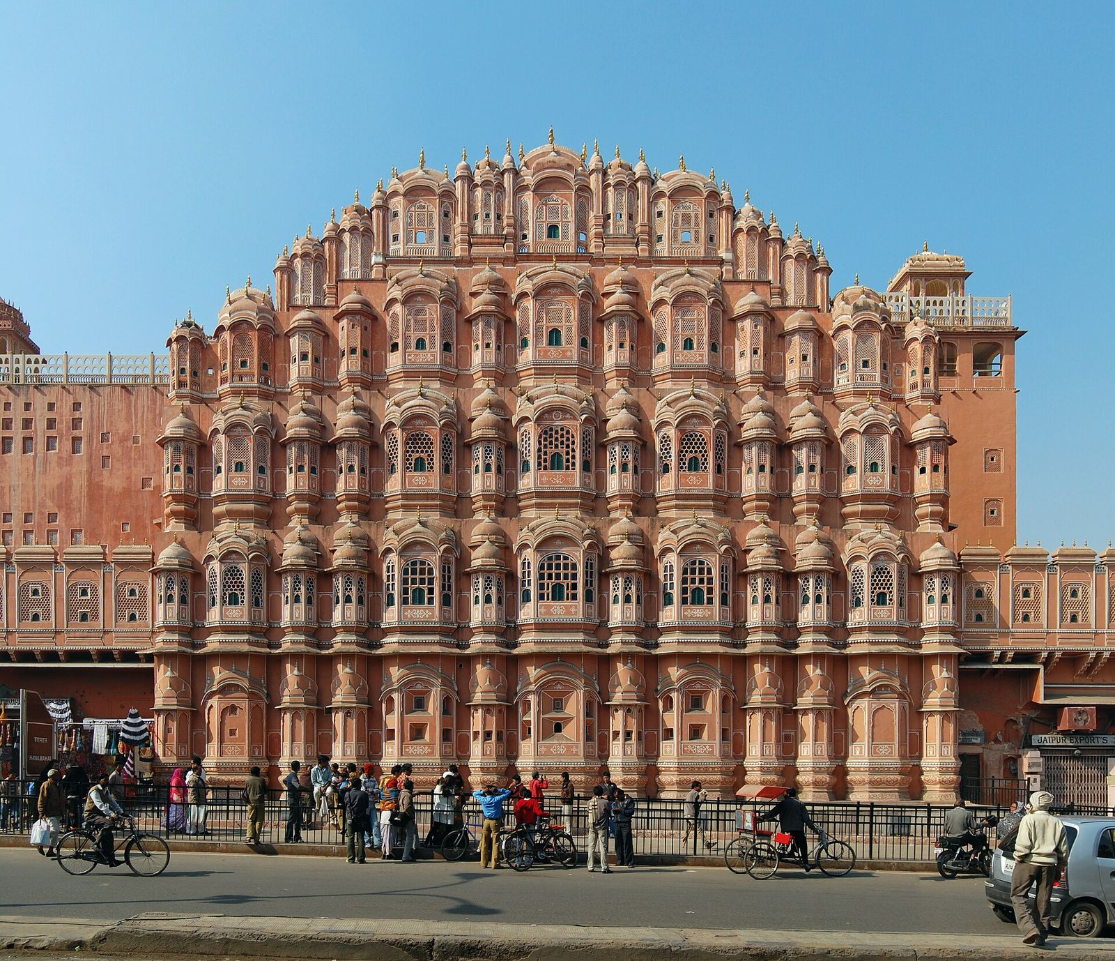 The pink sandstone face of the Hawa Mahal in Jaipur, cyclists on the road below
