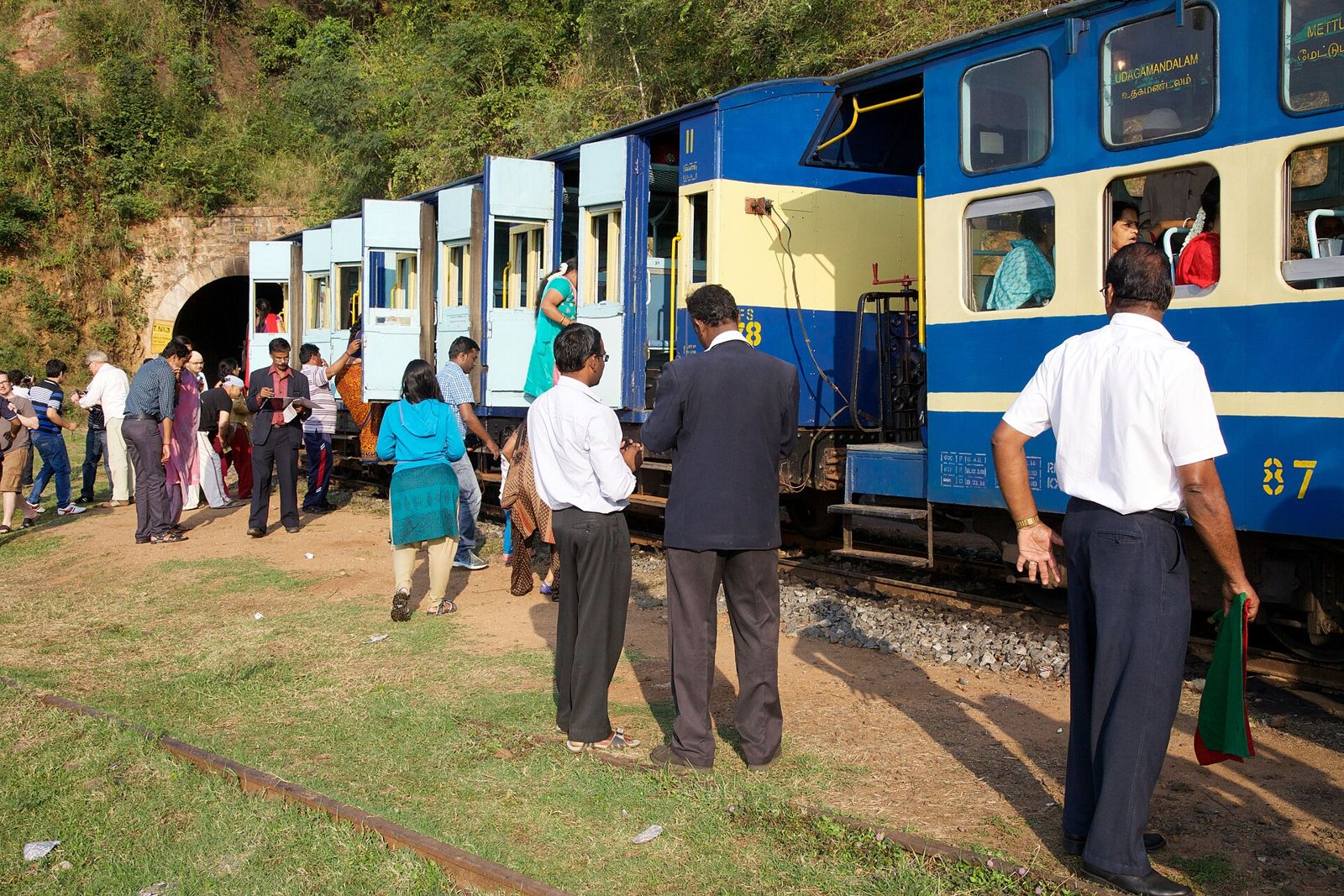 Passengers stretching their legs beside the blue Nilgiri Mountain Railway train